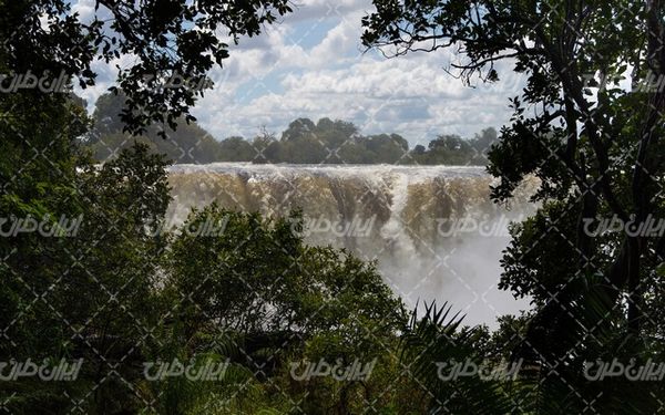 تصویر با کیفیت منظره زیبای آبشار به همراه آسمان ابری و درخت