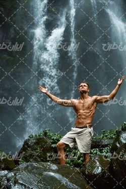 تصویر با کیفیت تناسب اندام مرد ورزشکار همراه با مرد و آبشار زیبا