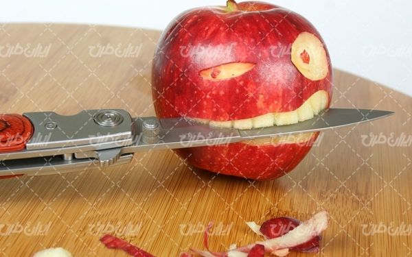 تصویر با هکاکی روی سیب قرمز همراه با چاقو و میوه